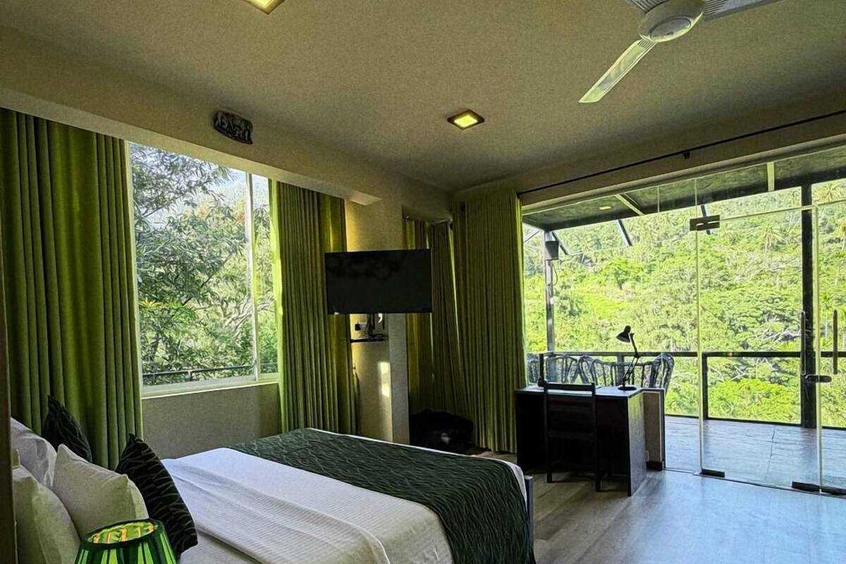 Quarto de hotel moderno com uma cama grande, uma escrivaninha, televisão e varanda com vista para o verde.