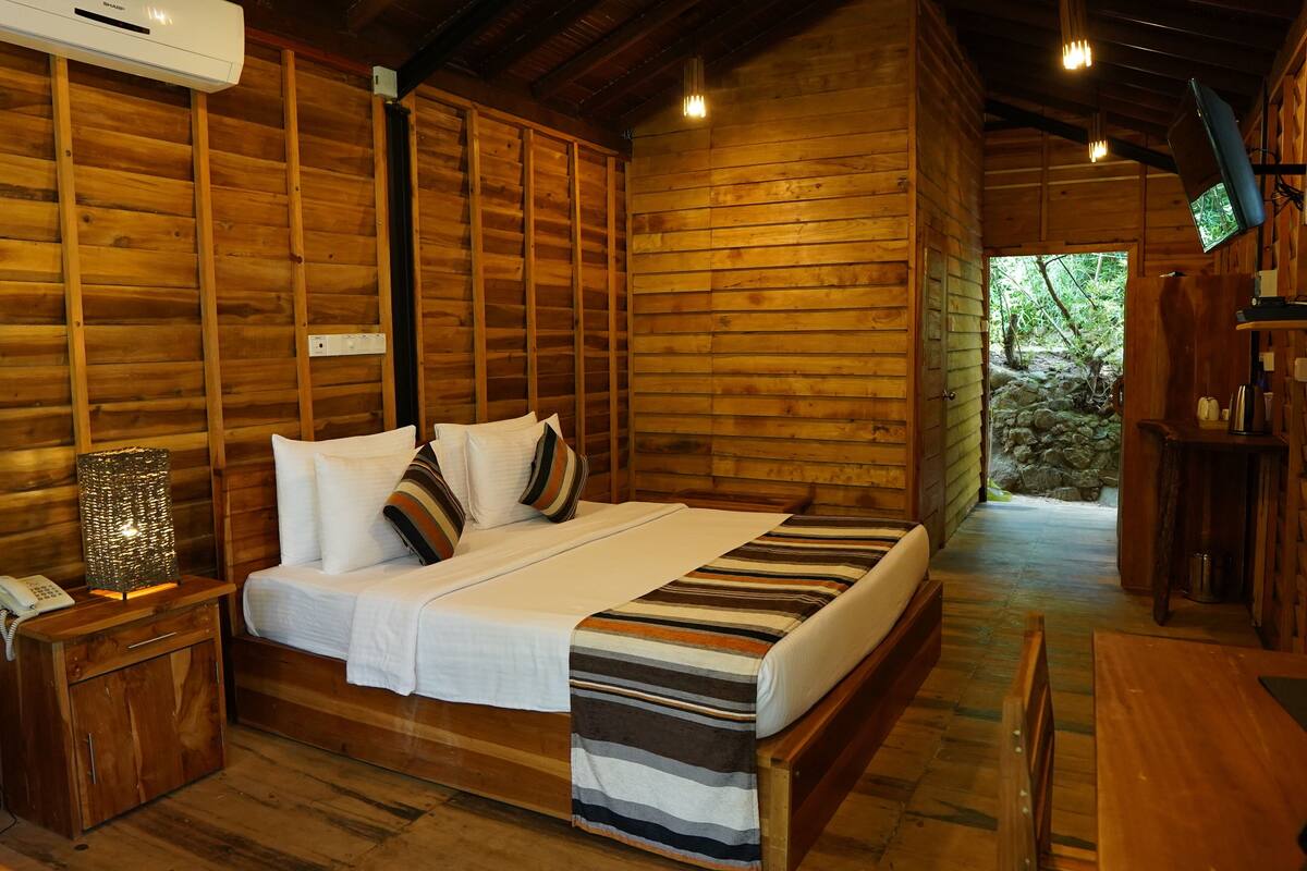 Quarto de cabana de madeira com cama, mesa de cabeceira e televisão na parede.