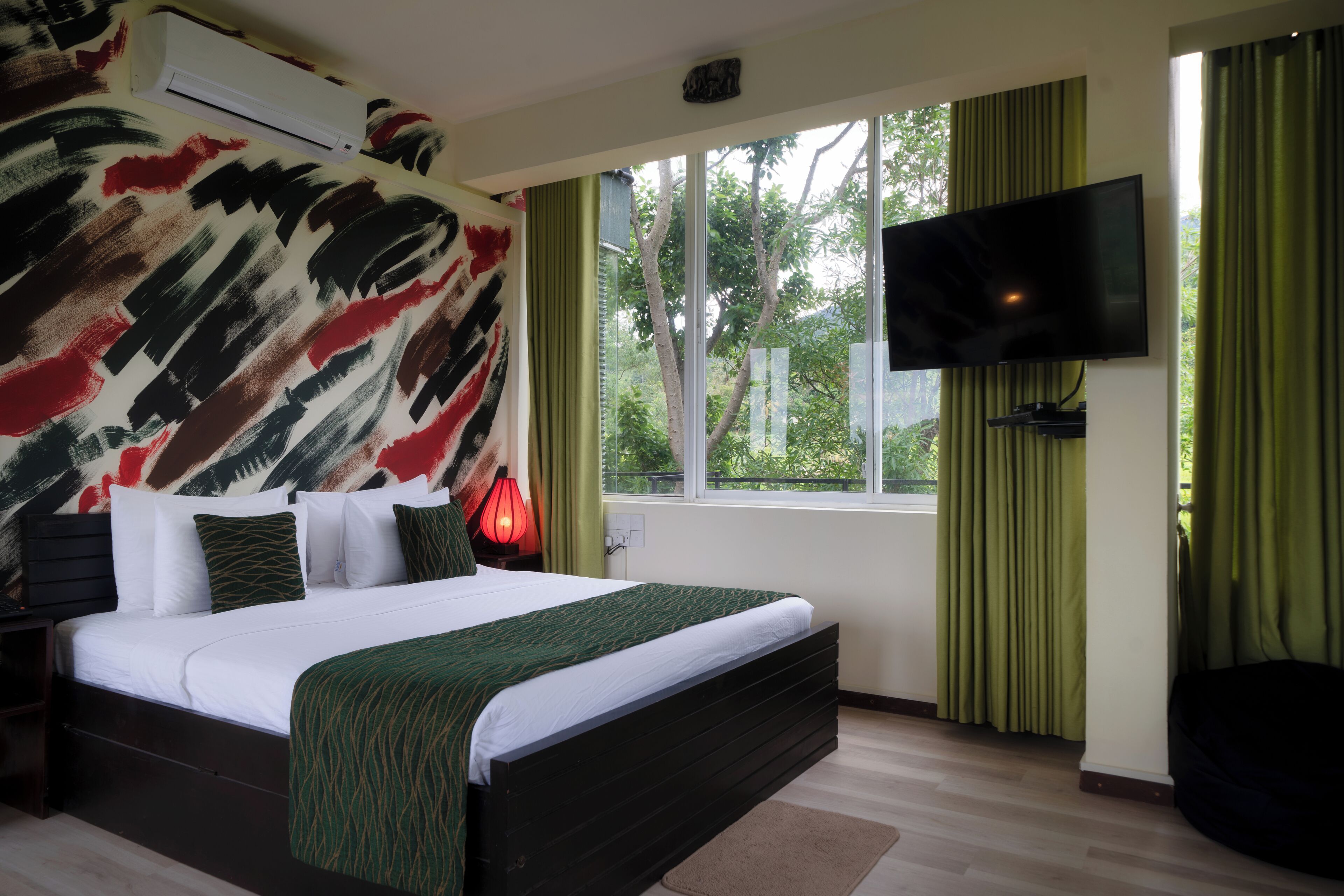 Een slaapkamer met een groot bed, een flatscreen televisie aan de muur en een raam met gordijnen.