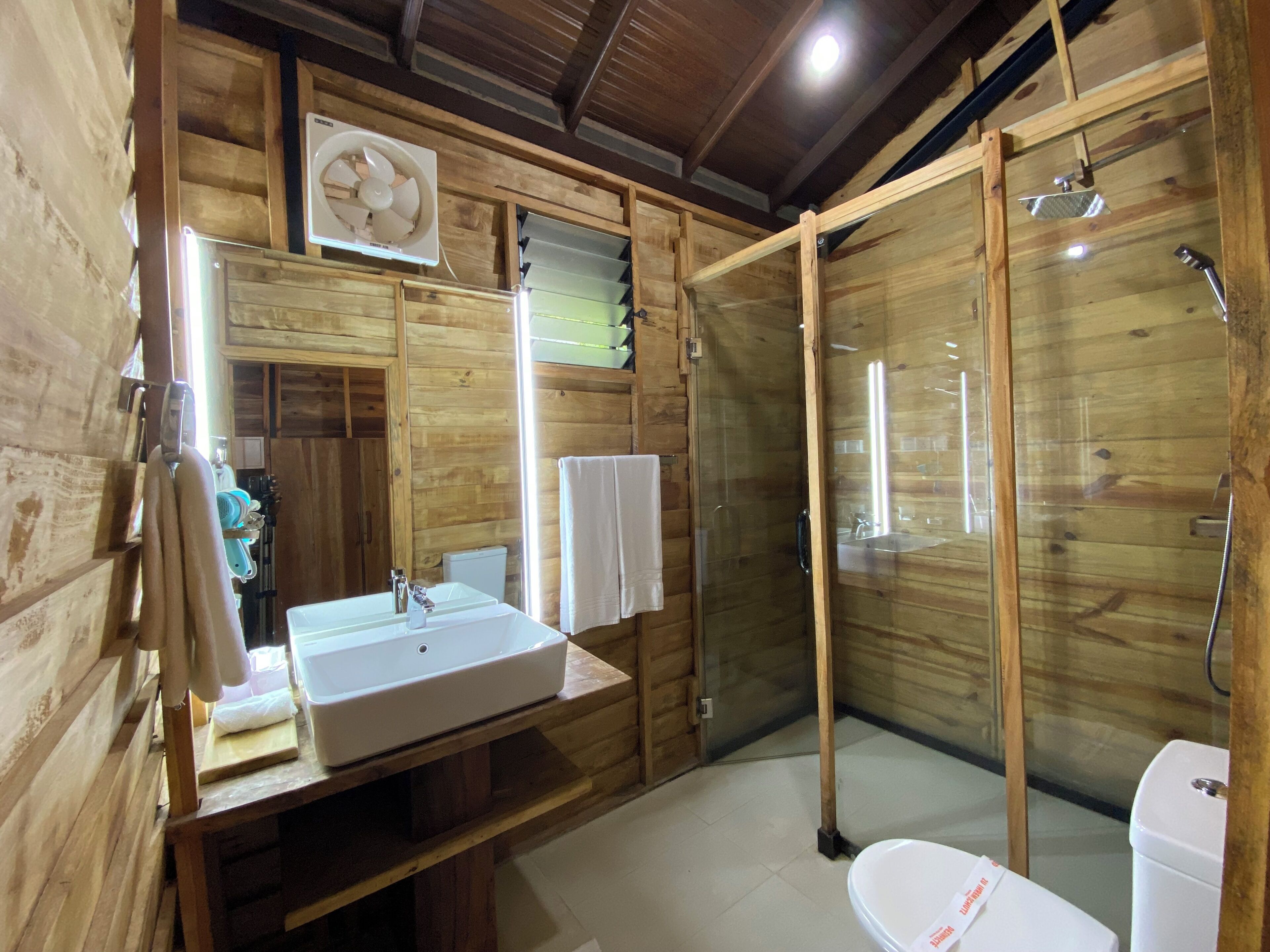 A wooden cabin bathroom with a sink, mirror, towel rack, and glass-enclosed shower.