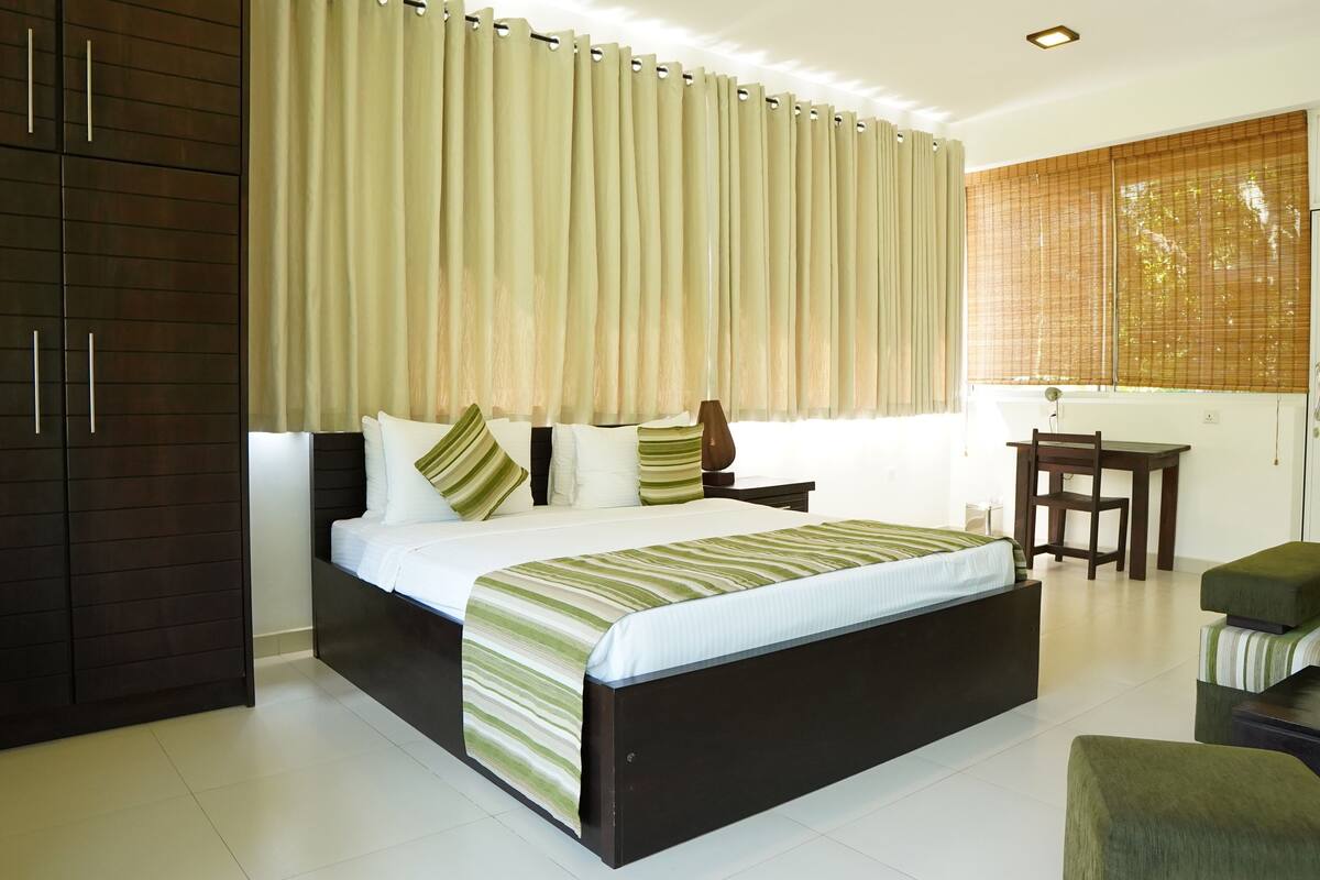 Quarto de hotel moderno com uma cama grande, um guarda-roupa de madeira, uma escrivaninha e uma cadeira.