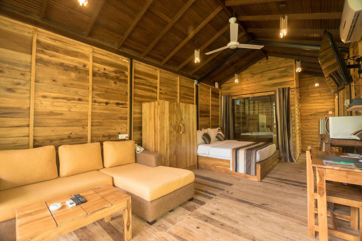 Interior em madeira com um sofá, uma cama, uma mesa e um ventilador de teto.