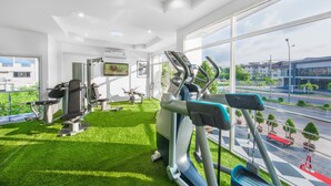 A gym with various exercise equipment, a large window with a city view, and artificial grass flooring.