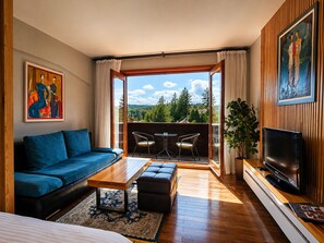 A modern living room with a sofa, coffee table, and TV, a balcony with chairs, and a painting on the wall.