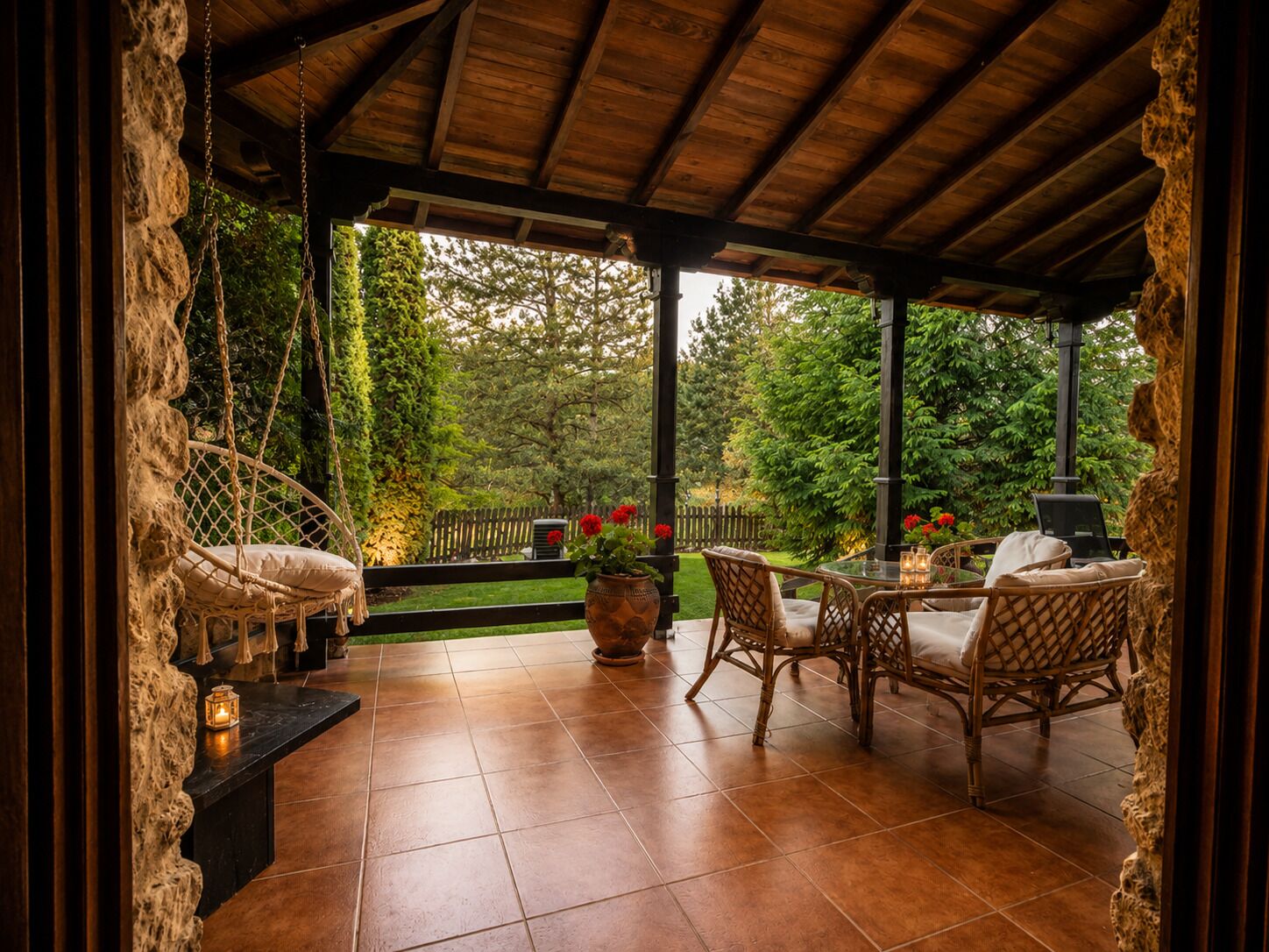 A covered patio with wicker furniture, a hanging chair, and a view of a garden.