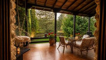 A covered patio with wicker furniture, a hanging chair, and a view of a garden.