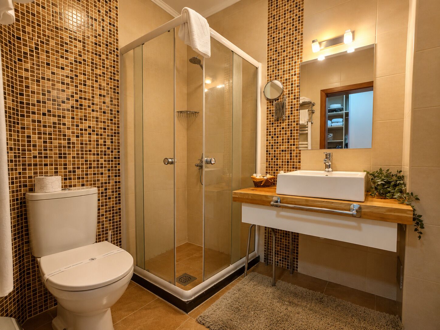Een badkamer met een douche met glazen wand, een toilet, een wastafel met spiegel en een betegelde muur.