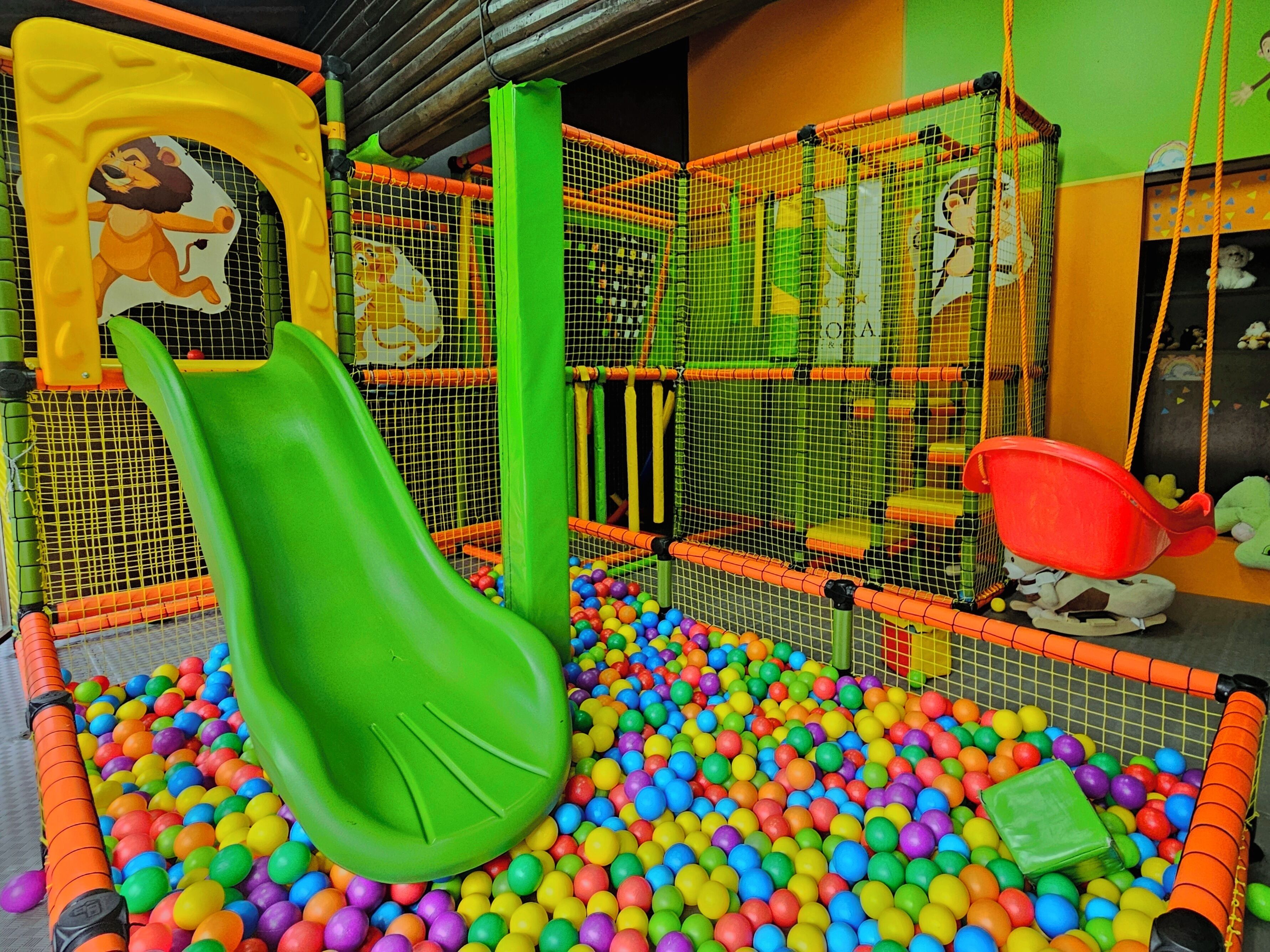 Un área de juegos con tobogán, estructuras de juego cubiertas por red y una piscina de pelotas.
