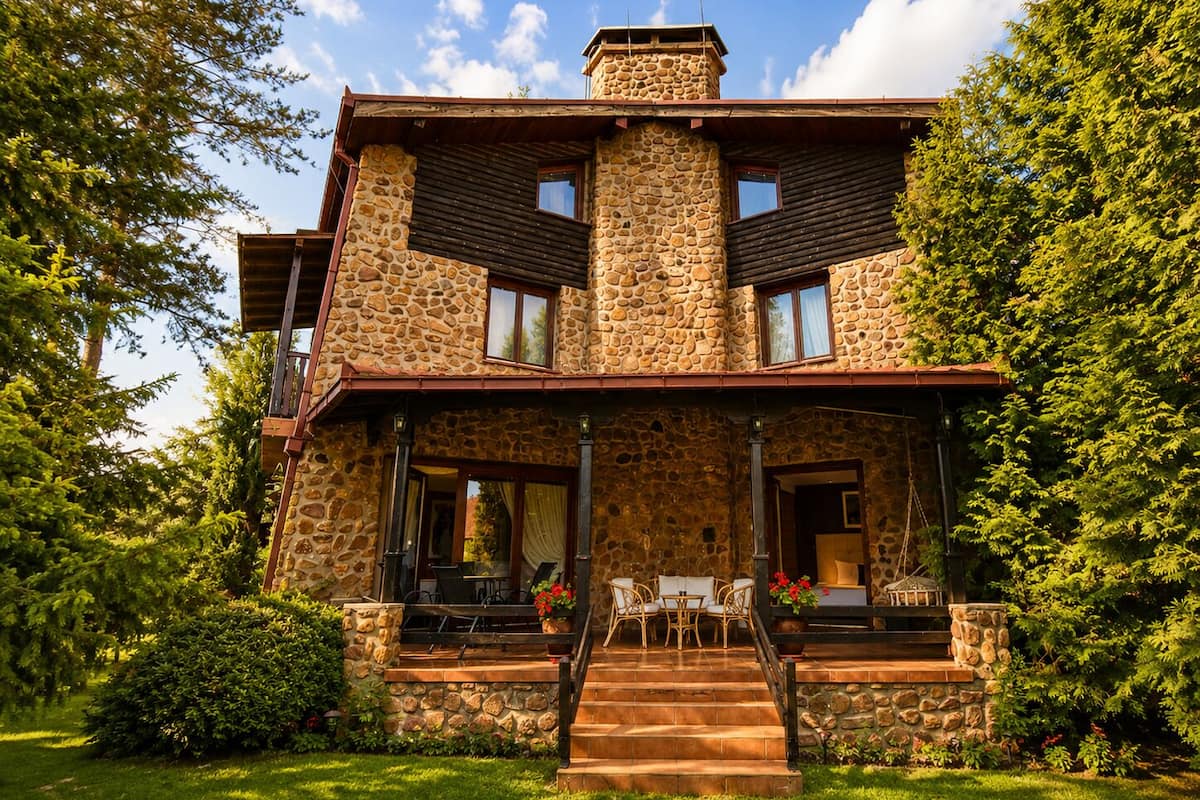 A stone house with a porch, outdoor seating, and a staircase leading to the entrance.