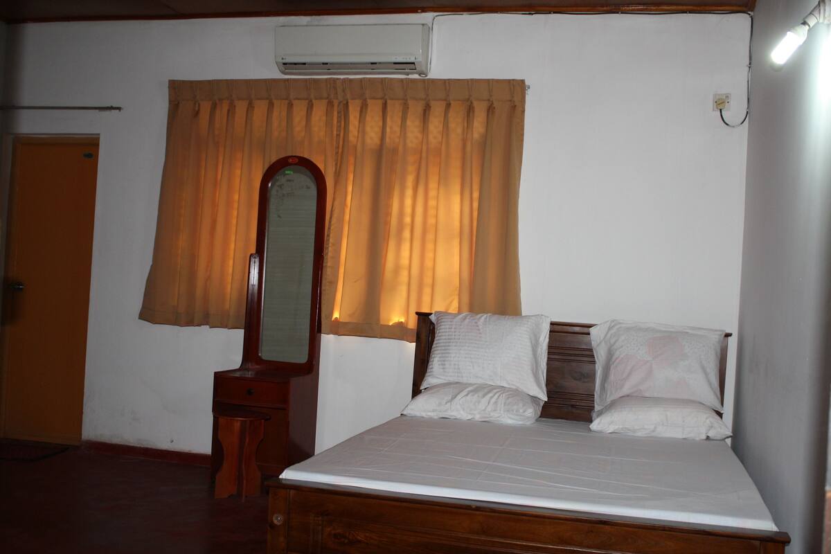 Une chambre à coucher avec un lit en bois, une table de chevet, un miroir et une fenêtre avec des rideaux.