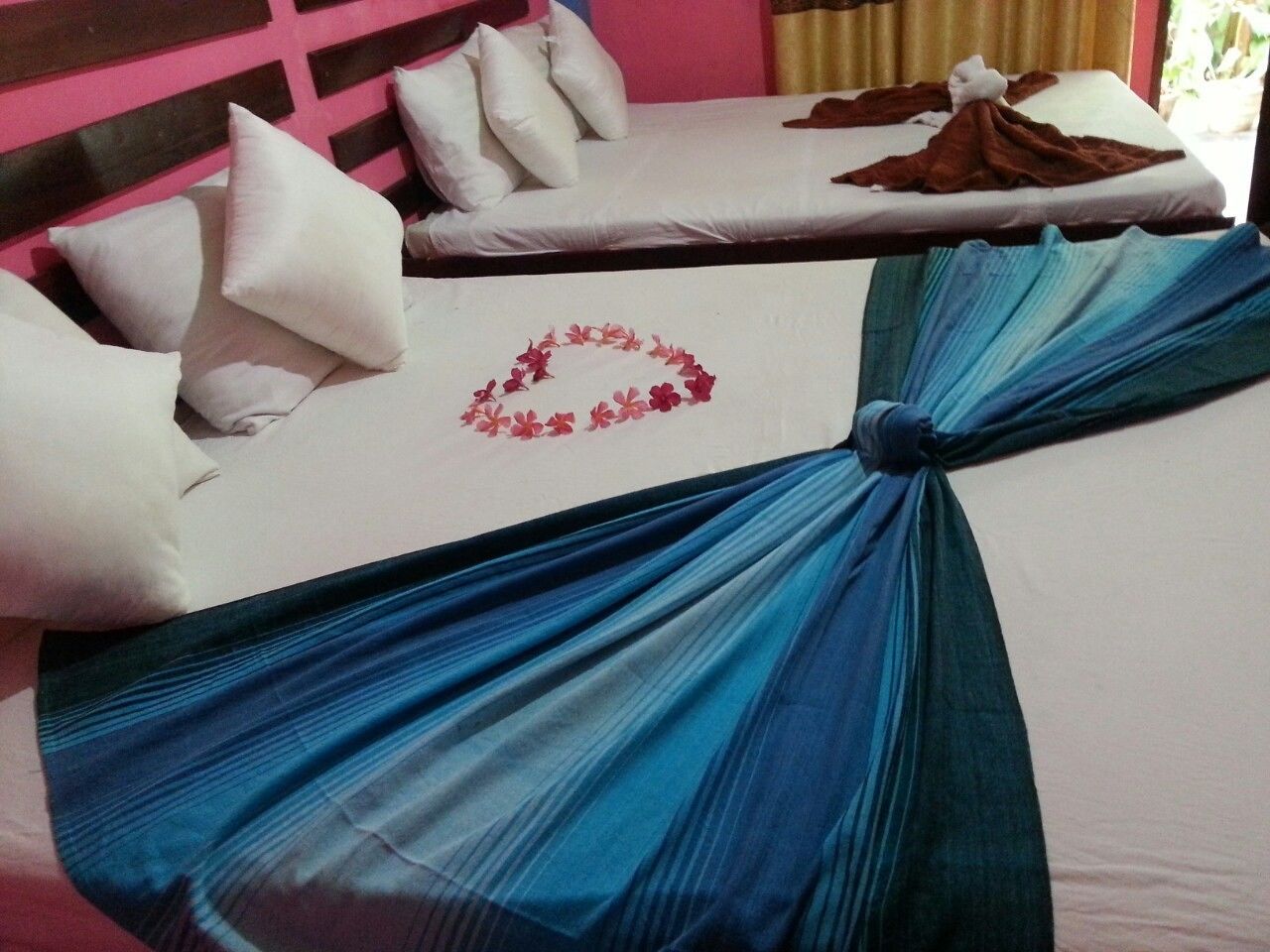 A hotel room with two beds, one with a blue draped bedspread and the other with white bedding and pillows.