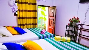 Habitación de hotel con dos camas, ropa de cama colorida, una mesita con un florero y vistas a zonas verdes.