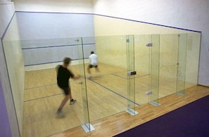A squash court with glass walls and a wooden floor.