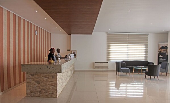 A reception area with a stone counter, two staff members, a sofa, and a window with blinds.