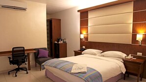 A hotel room with a bed, a desk, a chair, and a nightstand. - The Hub Hotel (Freetown)