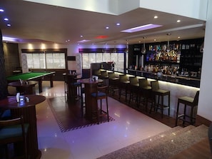 A bar area with a pool table, bar stools, and a bar stocked with liquor bottles.