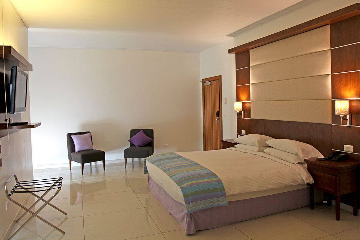 A hotel room with a bed, two chairs, a TV, a desk, and a lamp.