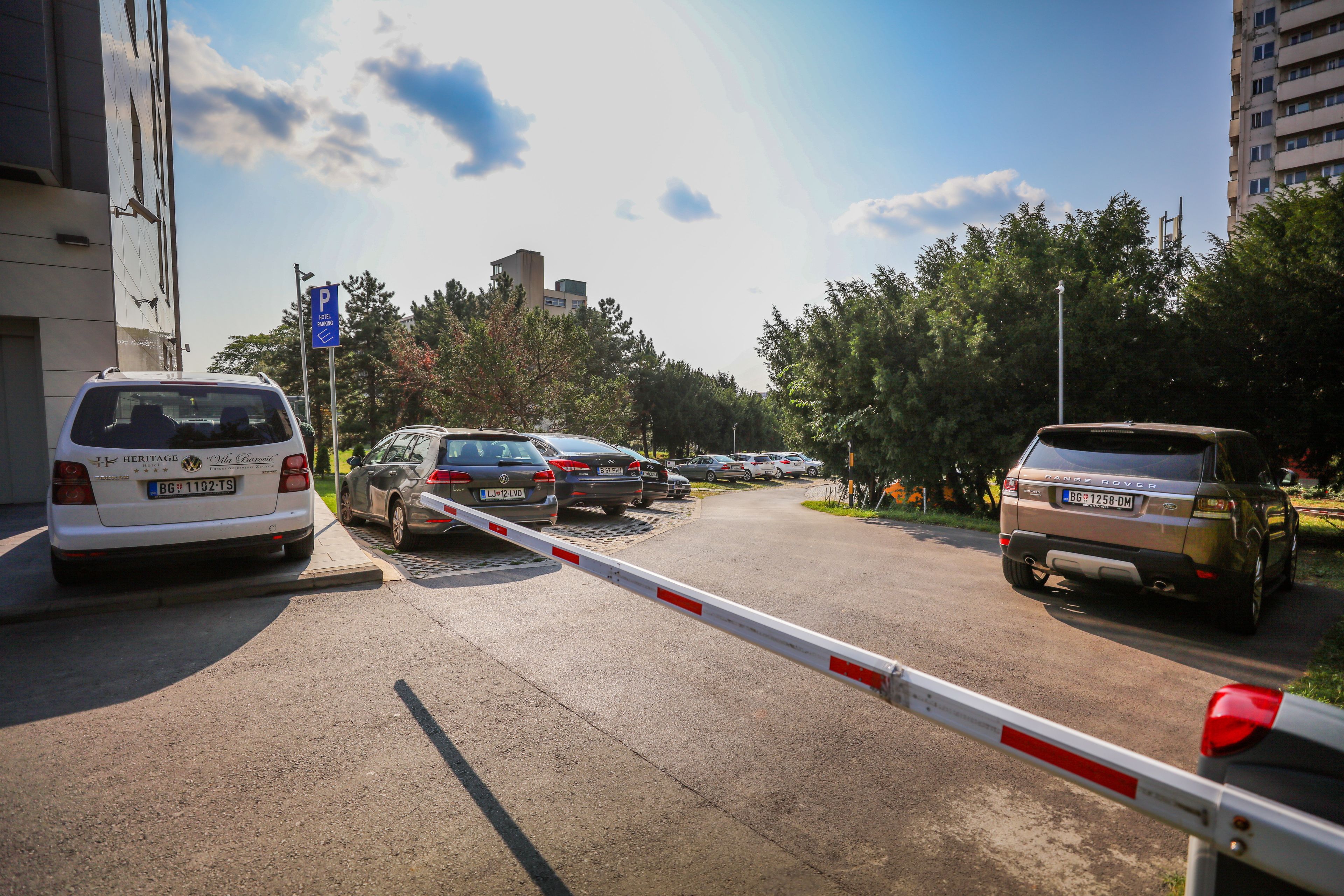 A street with cars parked on the side, a blue parking sign, and a barrier gate.
