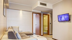 A modern hotel room with a white sofa, a flat-screen TV mounted on the wall, and a visible bathroom door. - Hotel Heritage (Belgrade)