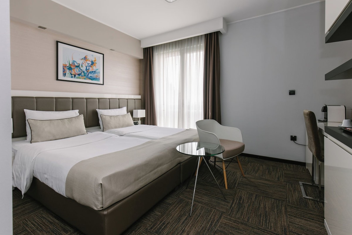 Una habitación de hotel con una cama, una silla, un escritorio y un cuadro en la pared.