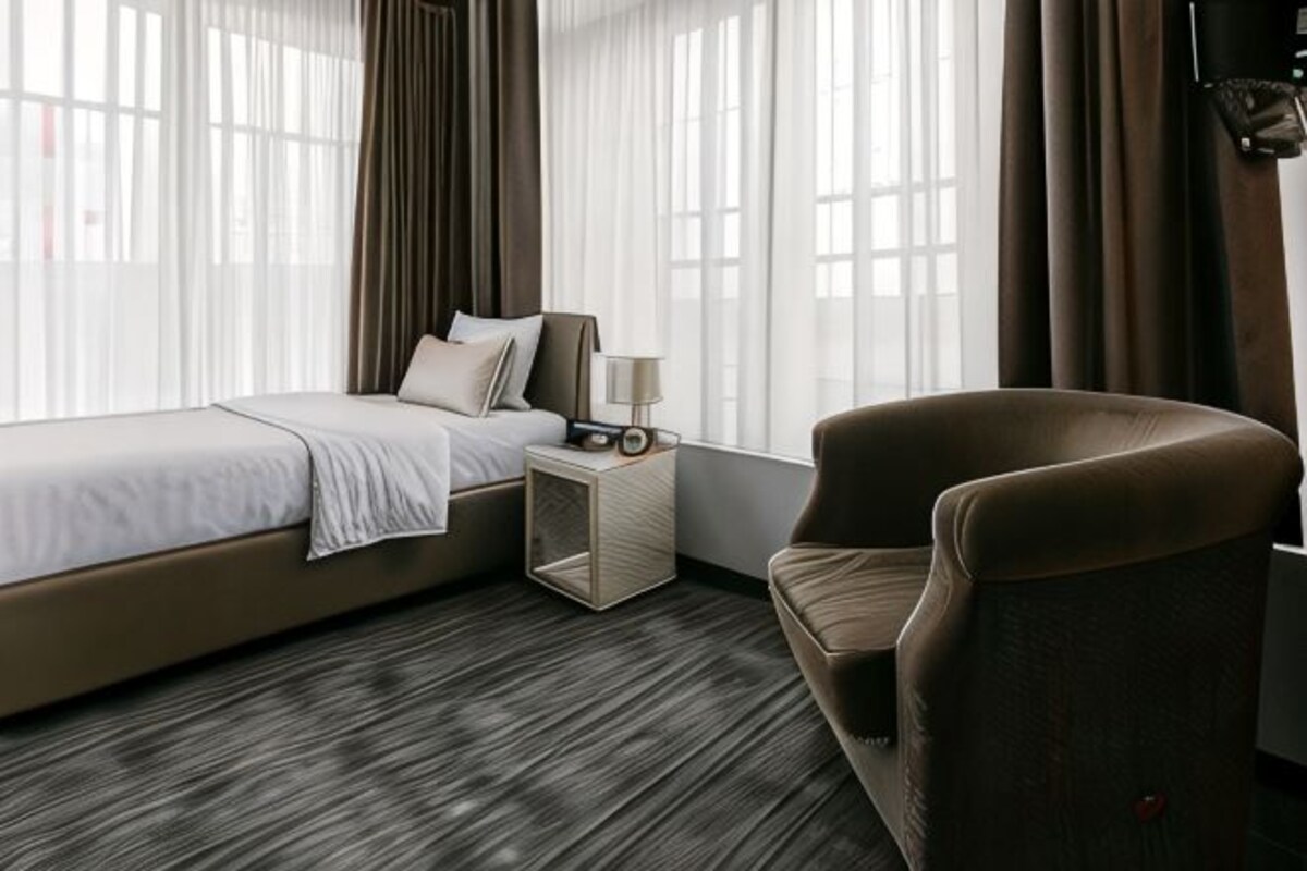 Una habitación de hotel con cama, mesita de noche, silla y ventana con cortinas.