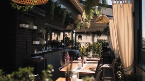 An outdoor dining area with wooden tables and chairs, hanging planters, and a brick wall. - Hotel Heritage (Belgrade)