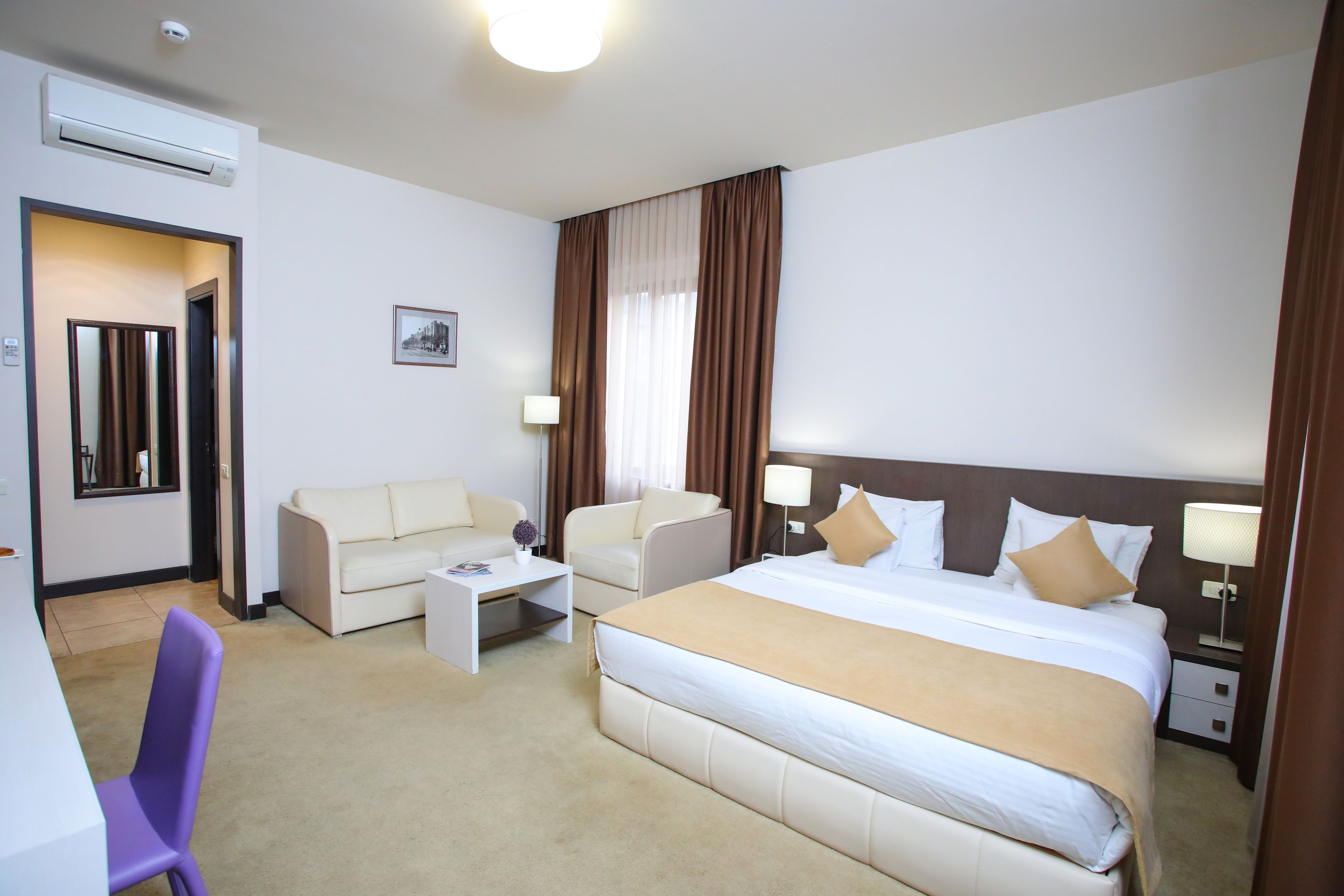 A hotel room with a large bed, two armchairs, a small table, and a desk.