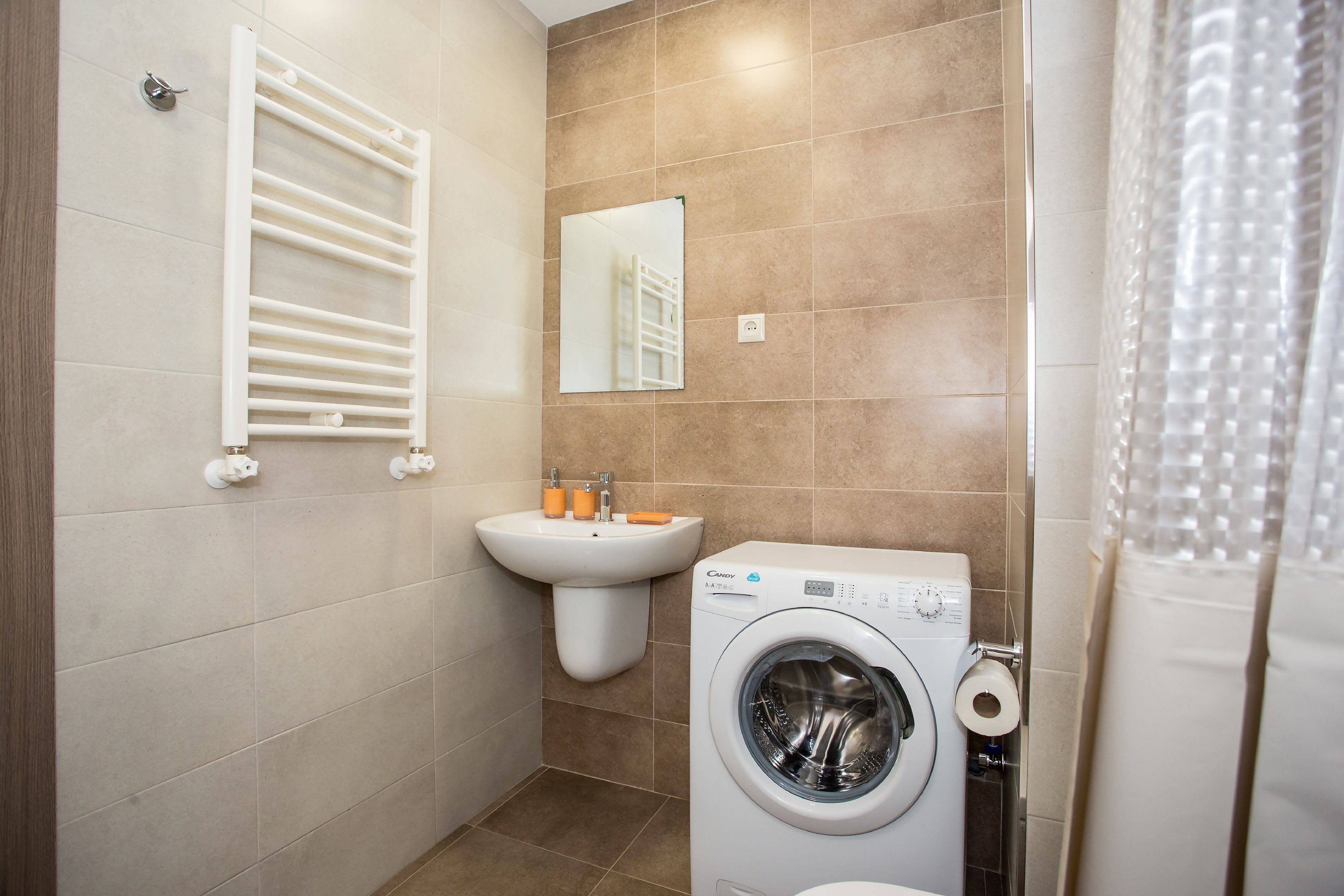 A compact bathroom with a built-in washing machine, a sink, and a towel rack.