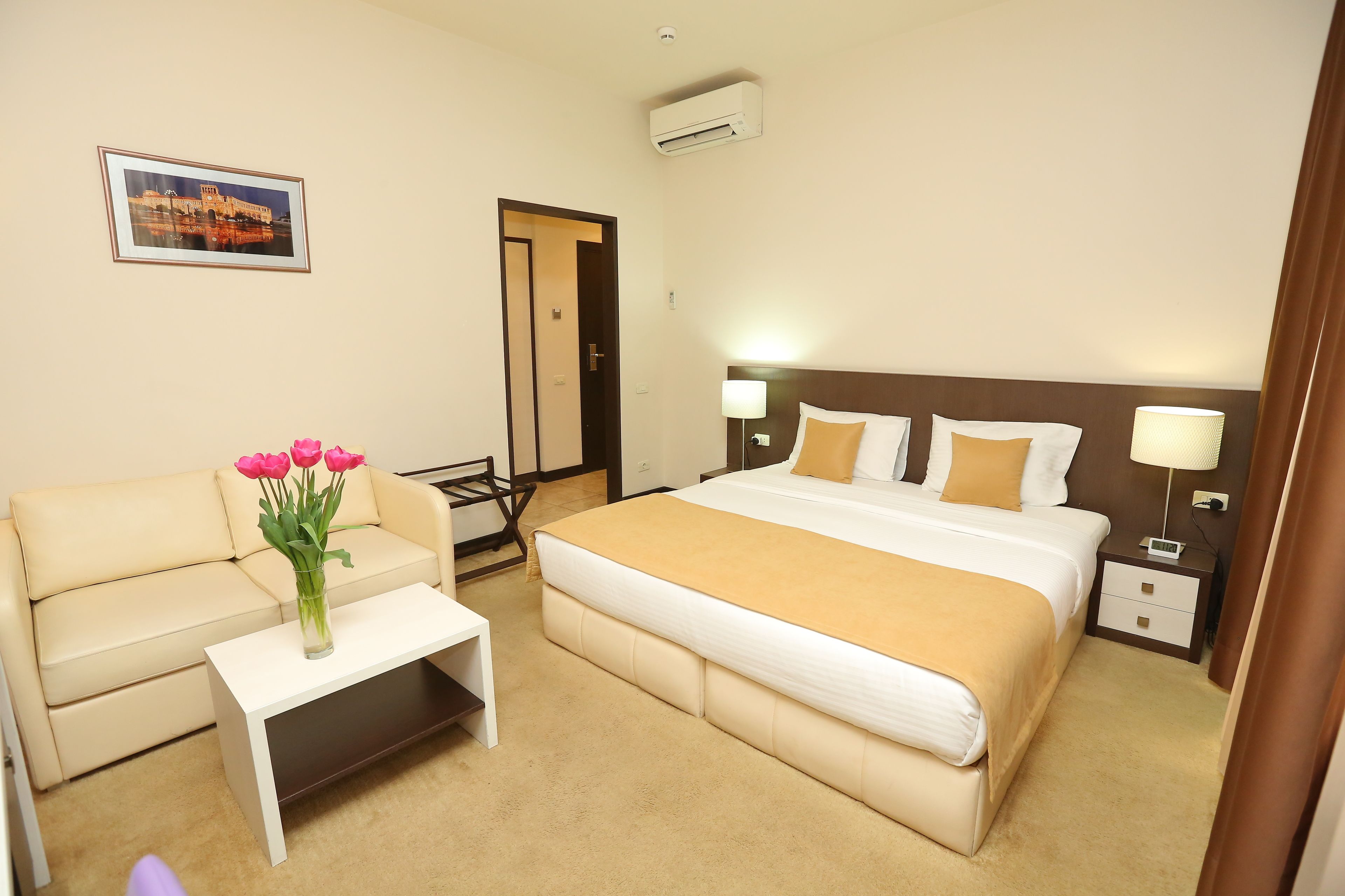 A hotel room with a bed, a sofa, a small table with a vase of flowers, and a picture on the wall.