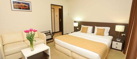 A hotel room with a bed, a sofa, a small table with a vase of flowers, and a picture on the wall.