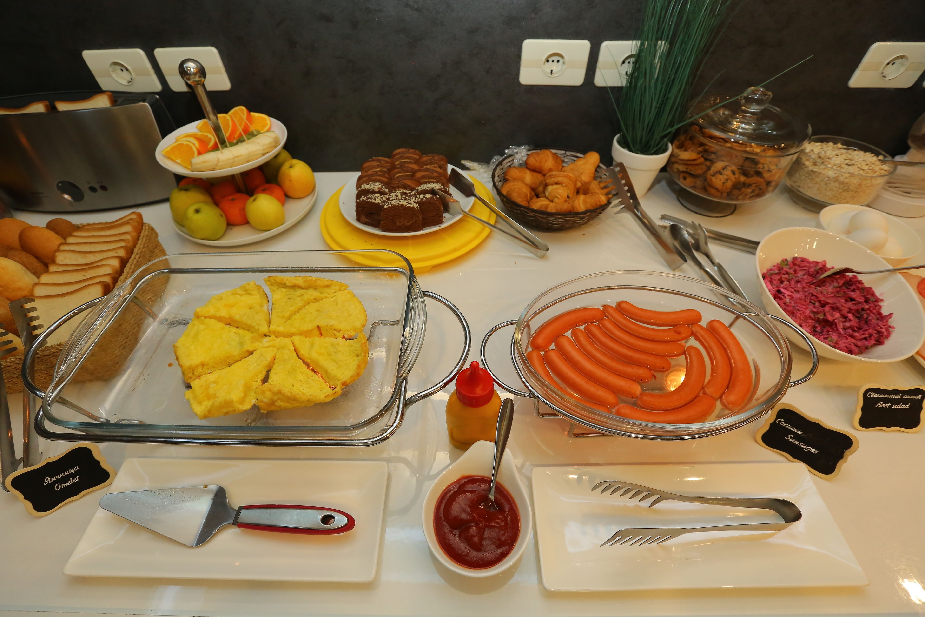 A buffet with various food items including sliced bread, eggs, sausages, and a variety of condiments.
