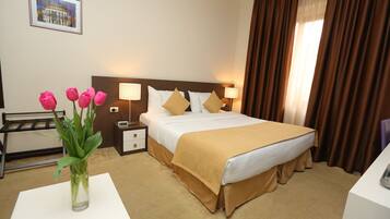 A hotel room with a bed, bedside tables, lamps, a vase with flowers, and a picture on the wall.