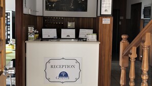 Un mostrador de recepción con un cartel que dice "RECEPTION", una imagen enmarcada de un paisaje urbano arriba y una escalera de madera a la derecha.