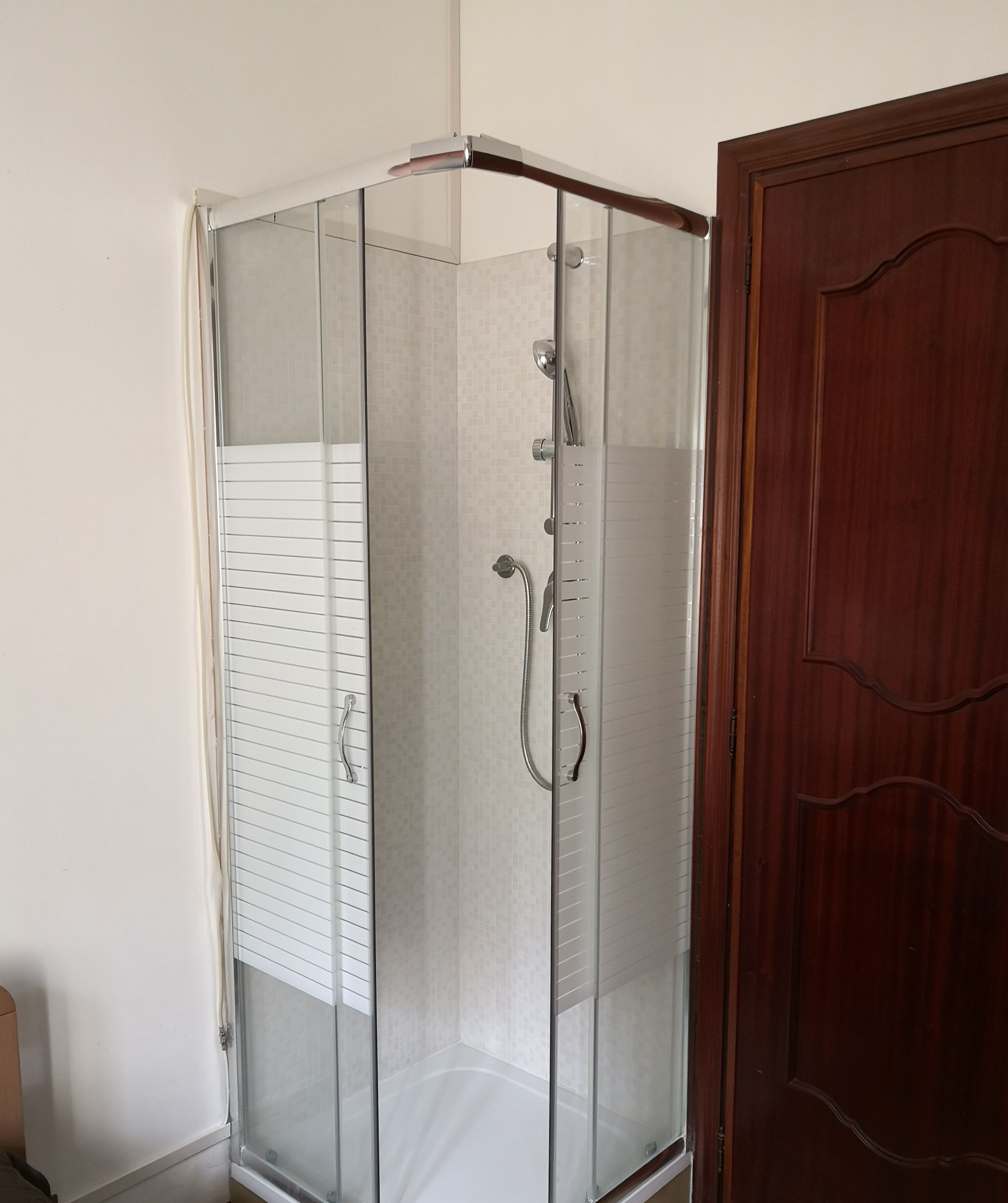 A glass-enclosed shower with a wooden door and a white towel rack.