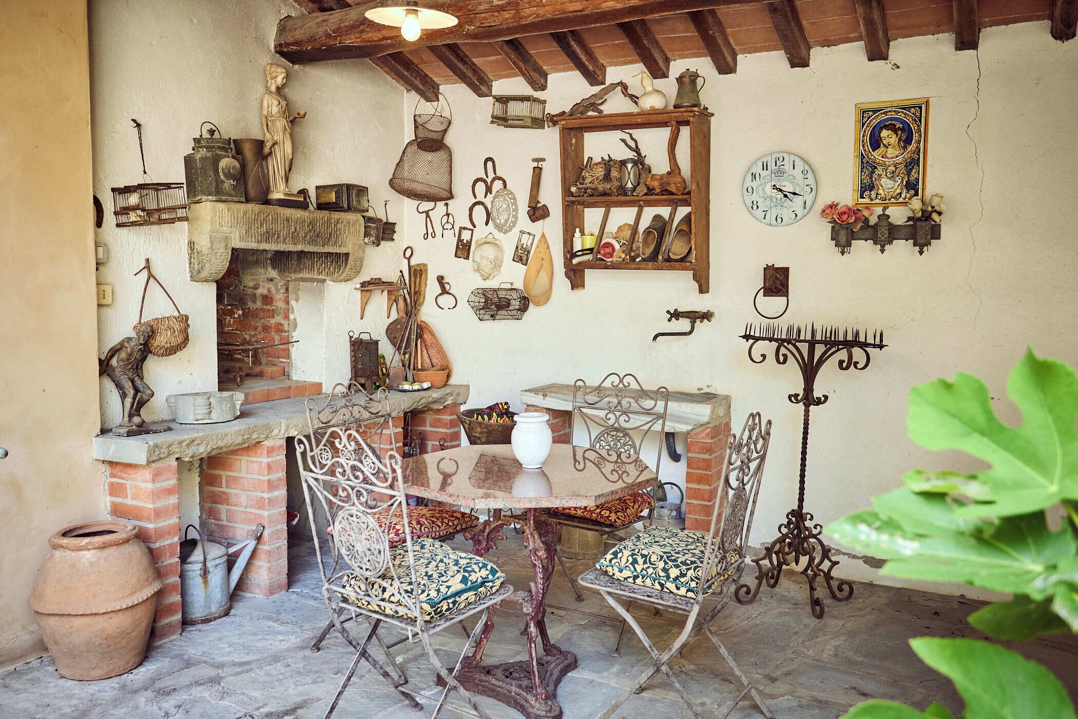 Un espace de restauration extérieur de style rustique, avec une cheminée en briques, des chaises en métal et divers ustensiles de cuisine et objets de décoration accrochés aux murs.