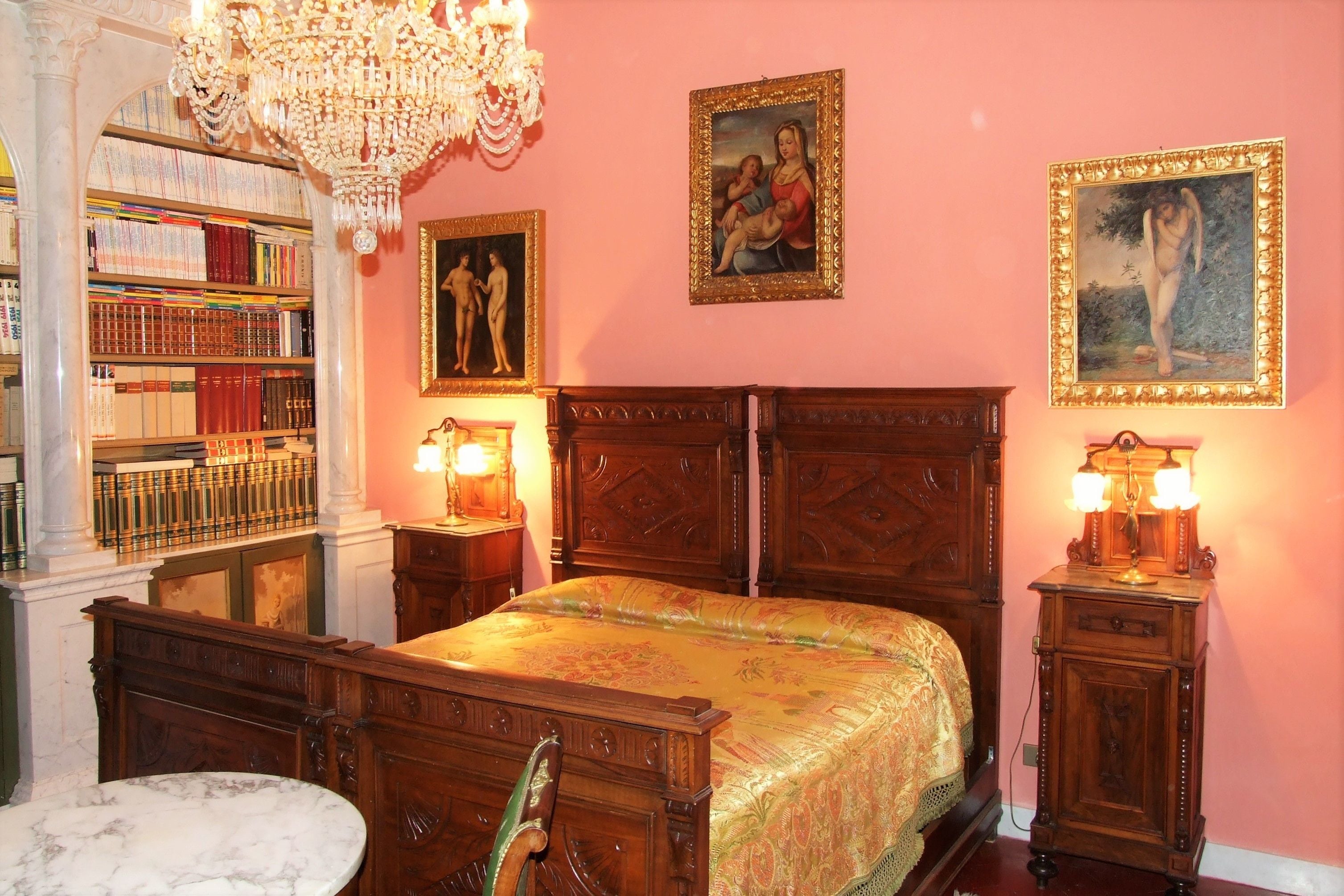 A bedroom with a large bed, a wooden headboard, a marble table, a bookshelf, and two wall-mounted lamps.