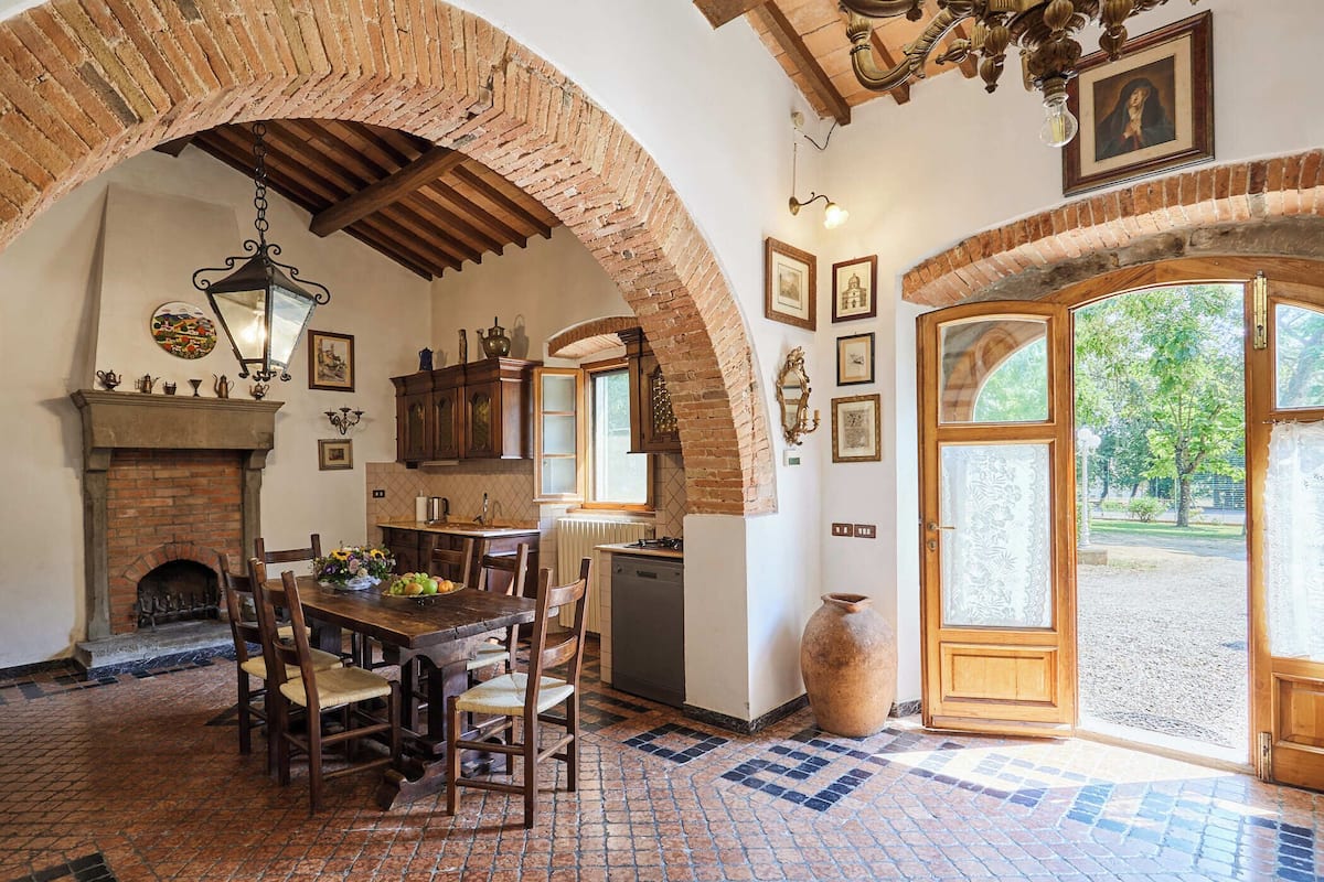 A rustic dining area with a brick fireplace, wooden table, and chairs.