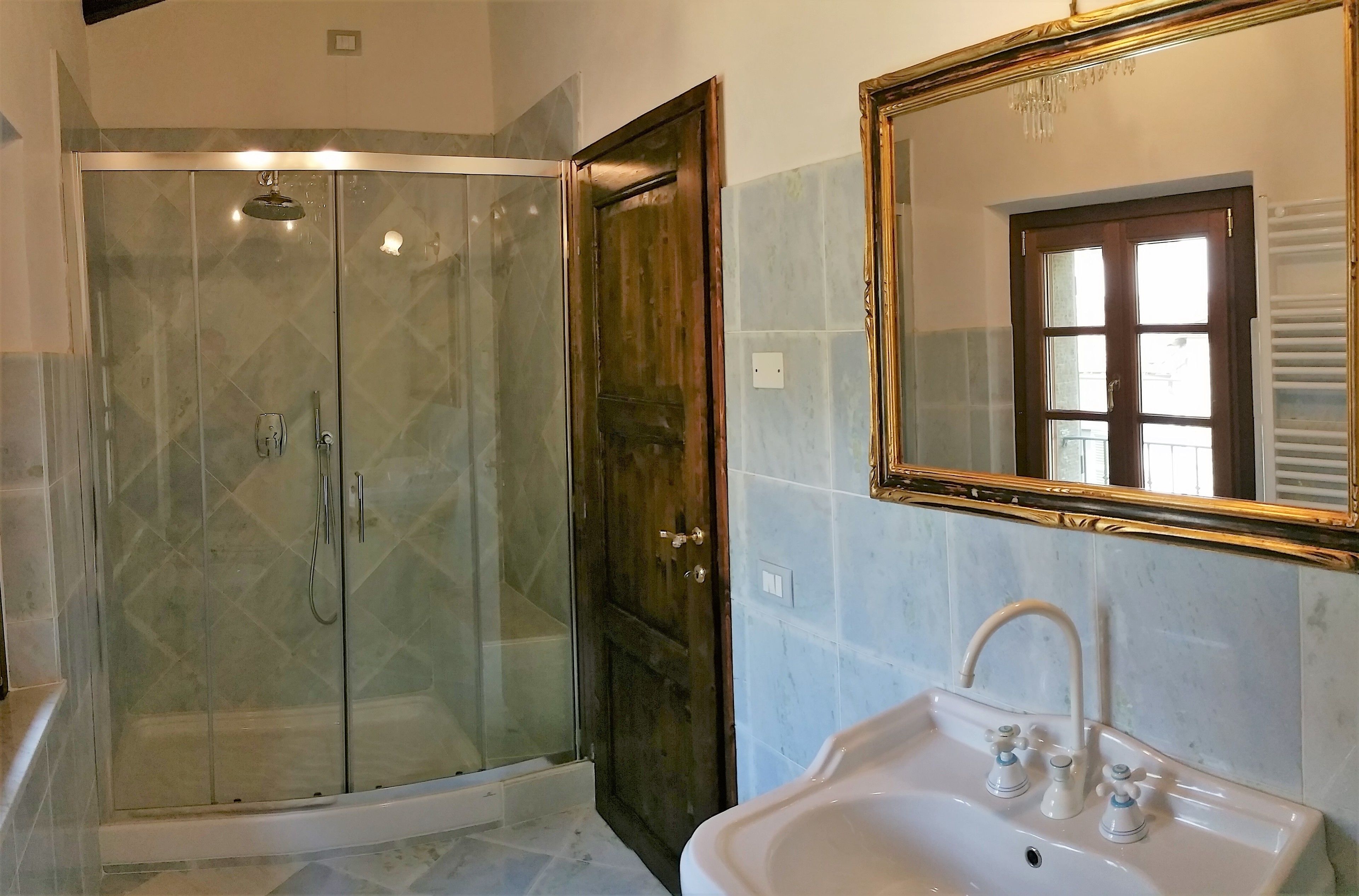 Une salle de bain dotée d’une douche à parois de verre, d’un lavabo avec deux robinets et d’un miroir avec un cadre doré.