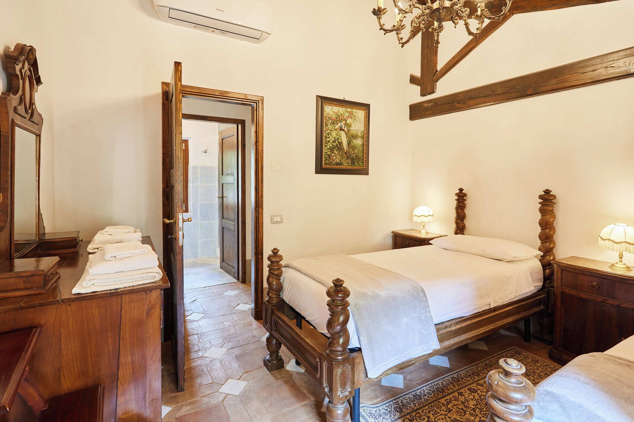 Un dormitorio con una cama de madera, una mesita de noche con lámpara, un aparador y un espejo.