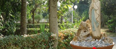 A statue of a woman in a garden setting with trees and a flower pot.