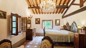 A bedroom with a wooden ceiling, a chandelier, a bed, a dresser, and a chair. - Agriturismo Villa Augusto (Cortona)