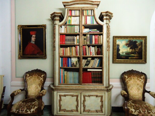 Una habitación con una amplia estantería, dos sillones decorativos, un retrato enmarcado y un cuadro de paisaje en la pared.