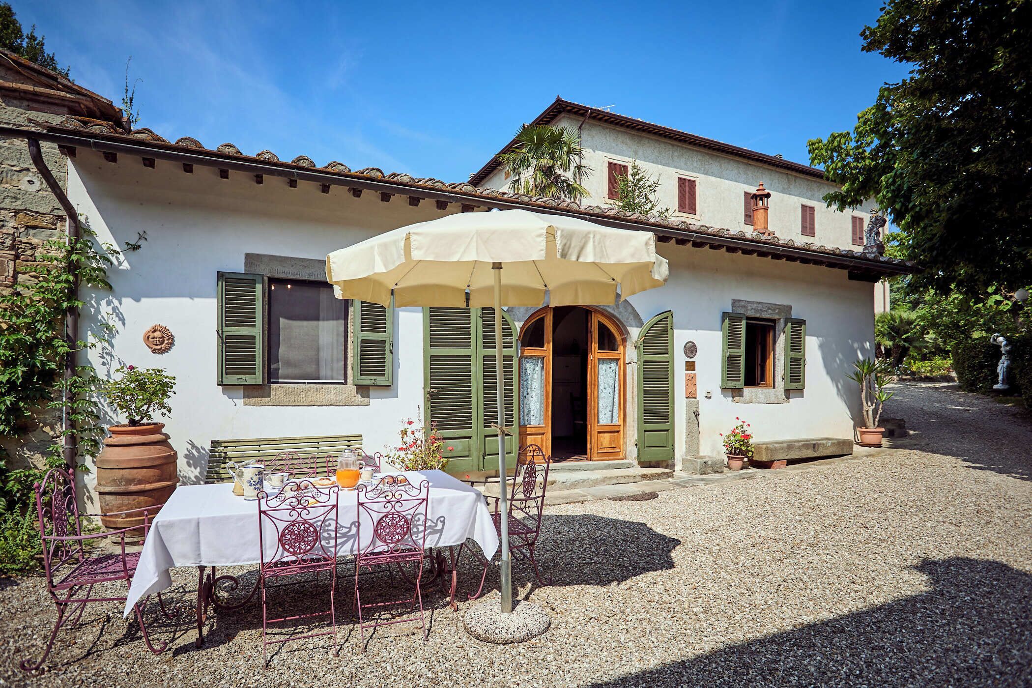 Une villa de style traditionnel avec une cour en gravier, une table avec des chaises et un grand parasol.