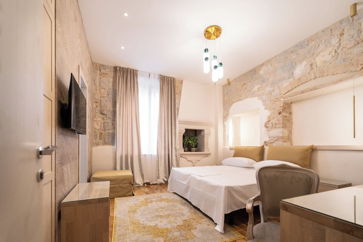 Habitación de hotel con pared de piedra, cama, escritorio, silla y televisor.