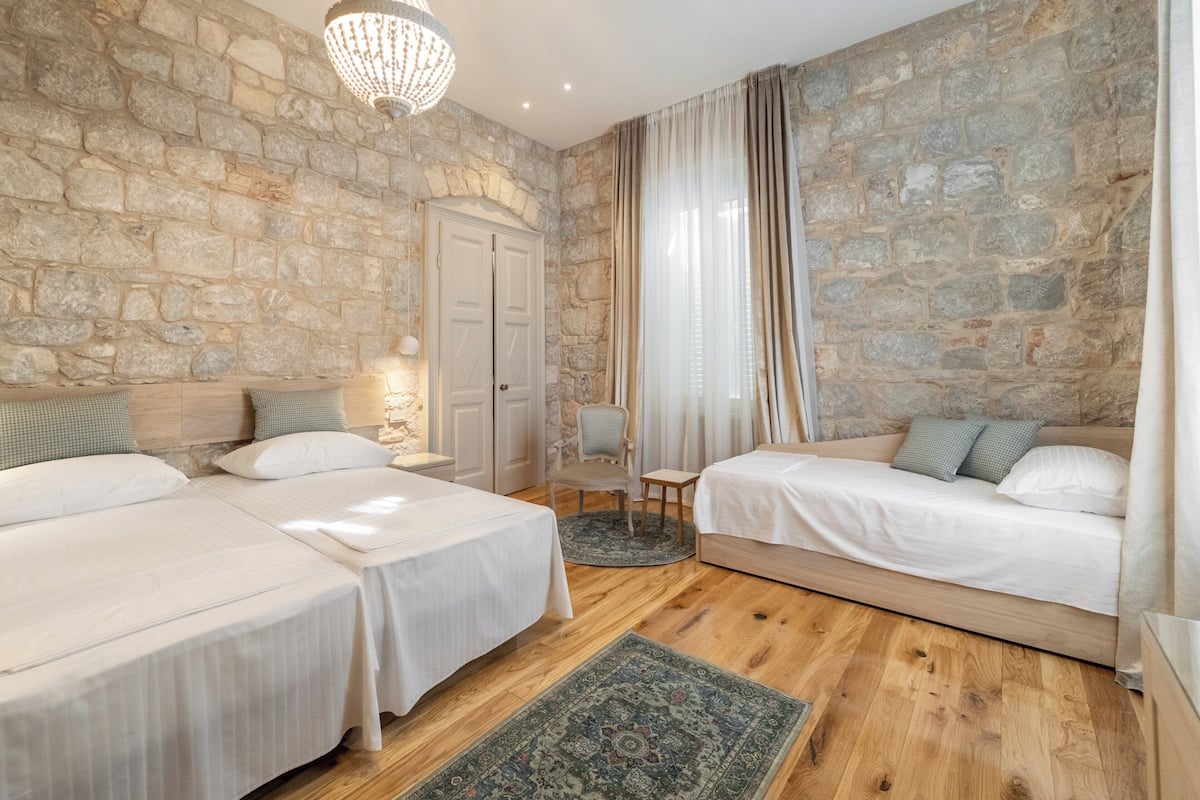 Una habitación con dos camas, una pared de piedra, un candelabro y una puerta.