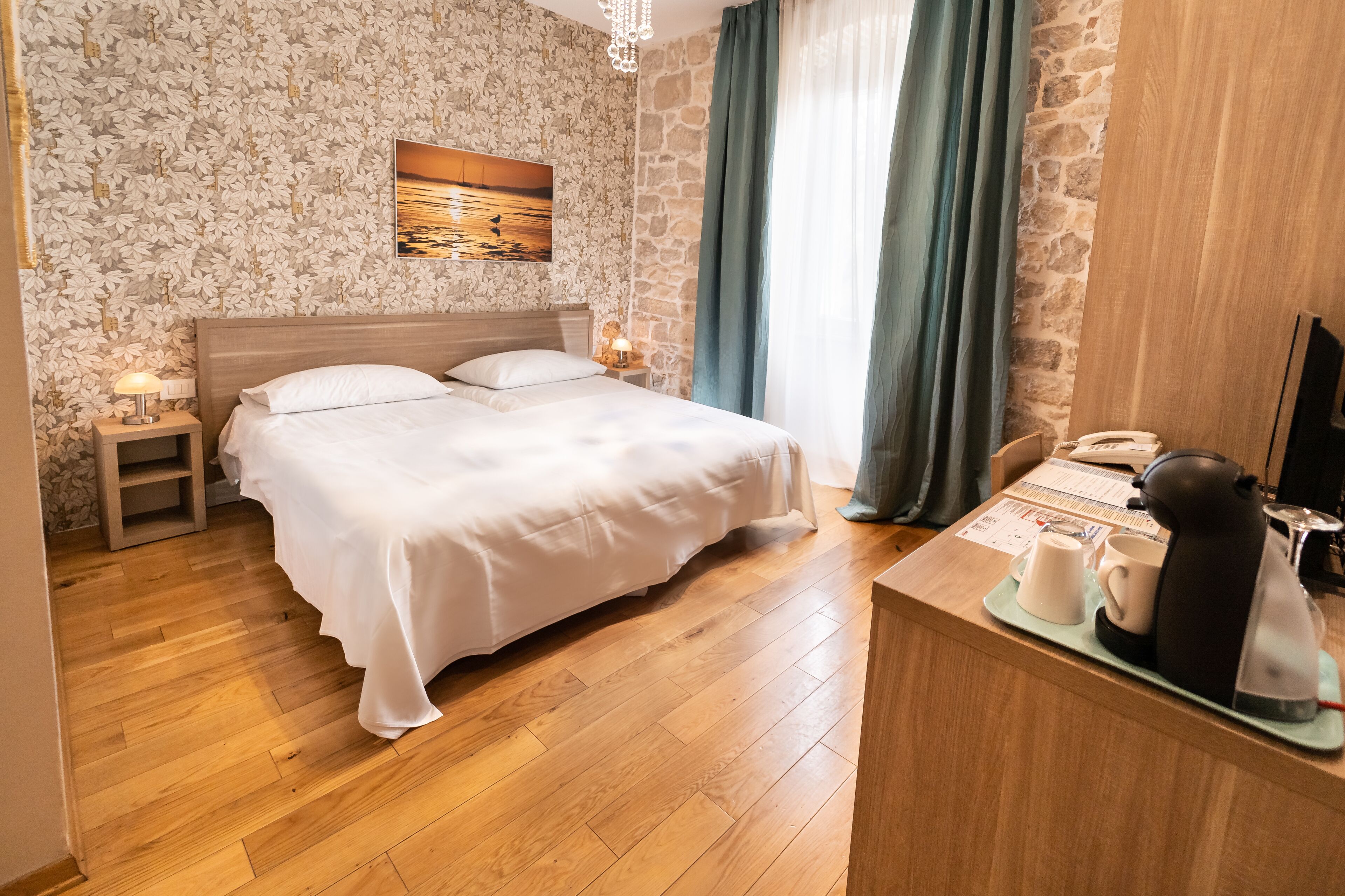 Une chambre d’hôtel avec un lit double, une petite table de chevet avec une lampe, une machine à café et un téléviseur posé sur un bureau en bois.