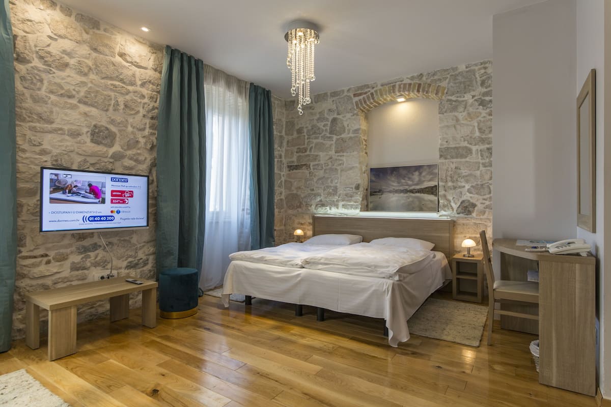 Un dormitorio con pared de piedra, una cama, mesitas de noche, un escritorio y un televisor mostrando una página web.