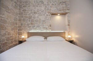 Ein Schlafzimmer mit Steinwand, einem Holzkopfteil, zwei Nachttischlampen und einem Bett mit weißer Bettwäsche.