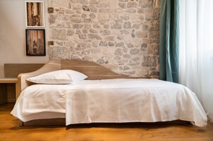 A bedroom with a stone wall, a wooden bed, white bedding, and two framed pictures on the wall.