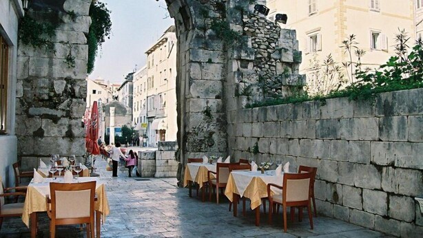 A narrow street with outdoor seating for a restaurant, stone walls, and buildings in the background. - Tifani Luxury Rooms 2 (Split)
